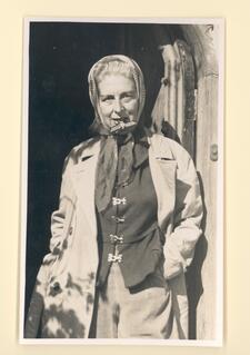 black and white photograph of an older person wearing a kerchief with a German soldier's badge in their teeth 