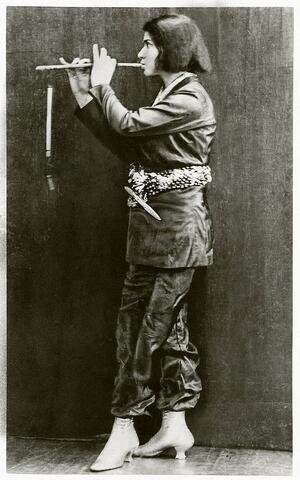 Else Lasker Schuler dressed in men's clothing with a decorative belt, playing a pipe