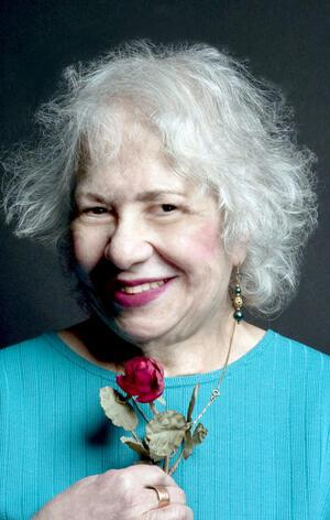 Aviva Cantor wearing a blue shirt holding a rose and smiling to the camera