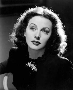 Hedy Lamarr in a long sleeved black dress with a brooch, seen from the chest up in the film The Heavenly Body