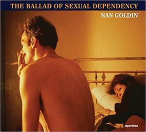 A book cover with a photo of a woman in a dark shirt lying on a bed with her head on a pillow, looking at a topless mad sitting on the edge of the bed and smoking a cigarette, facing away from the camera