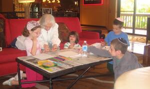 Grandmother coloring on paper with her grandchildren. They sit on and around a red couch.