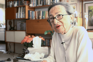 Vele Zabludovsky sitting in a living room, with a microphone clipped to her sweater