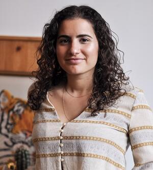 Erez Zobary is smiling at the camera, she has curly brown hair and is wearing a striped top.
