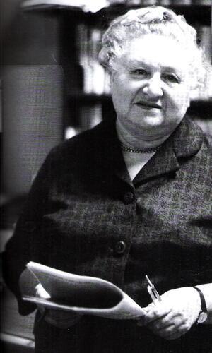 black and white photograph of an older woman with white hair holding a newspaper