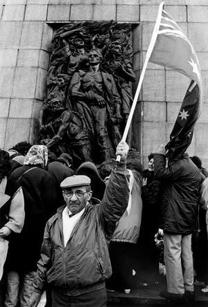 Man waving flag in front of Warsaw Ghetto Memorial with others in background, 1993