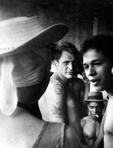 Black-and white-photograph of three men looking at a woman, whose back faces the camera