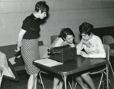 Black and white photo of three women at a table with a typewriter