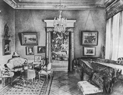 A small room with a chandelier, paintings, and upholstered antique furniture.