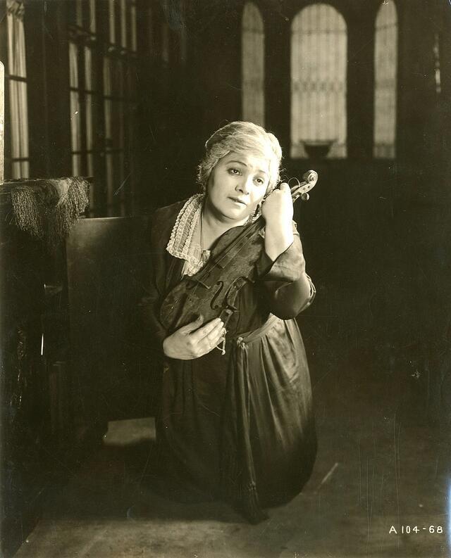 Vera Gordon cradling a violin in her arms close to her face