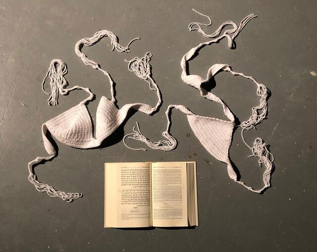 Installation of crocheted white bra and underwear with a prayer book, on a dark background