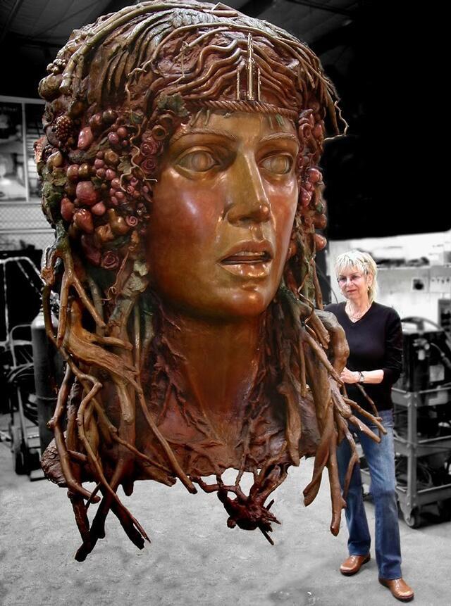 Audrey Flack in foundry standing beside a large bronze sculpture of the head of Daphne