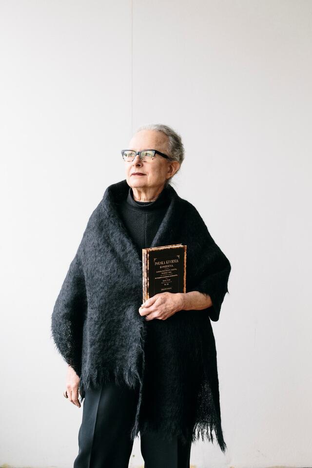 Barbara Kirshenblatt-Gimblett dressed in all black holding a book against a white background