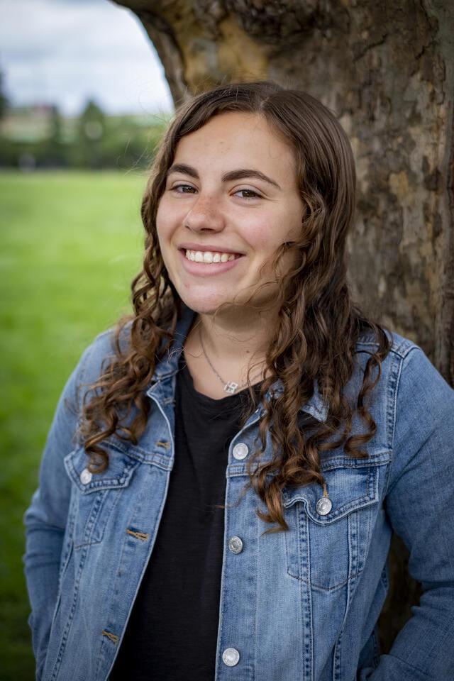 Photo of Ari Fogel, in front of a tree wearing a black shirt and a jean jacket