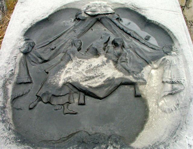 A gray stone, carved with the image of three women, a bed, and parted curtains