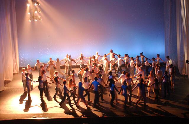 Large group of dancers in white clothing forming circles and holding hands for The Hallelujah Project