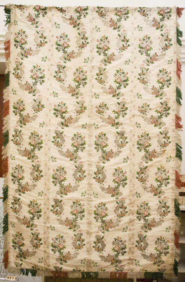 An off-white curtain embroidered with pink flowers, with fringe along the edges