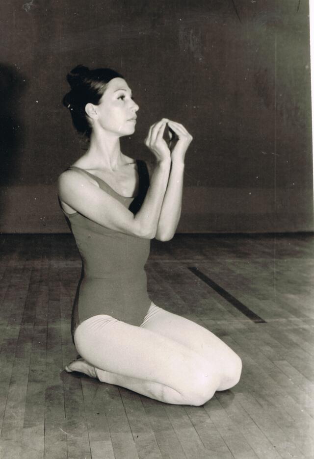 Ruth Eshel kneeling on a stage with her hands cupped in an oval shape