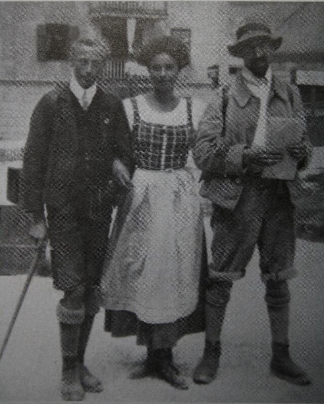 Emmy Eisenberg, arms linked with two men, all wearing boots, stockings, and short pants/a shorter skirt