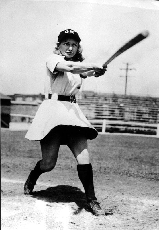 Thelma Eisen swinging a bat, wearing a skirted baseball uniform and a hat reading "GR"