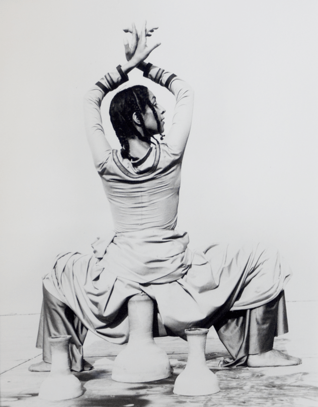 Ze'eva Cohen dancing, squatting low over some pieces of pottery with her wrists crossed above her head