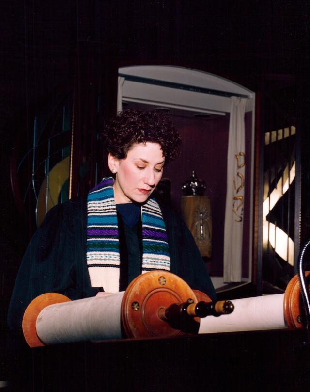 image of a dark-haired woman with a tallit reading Torah