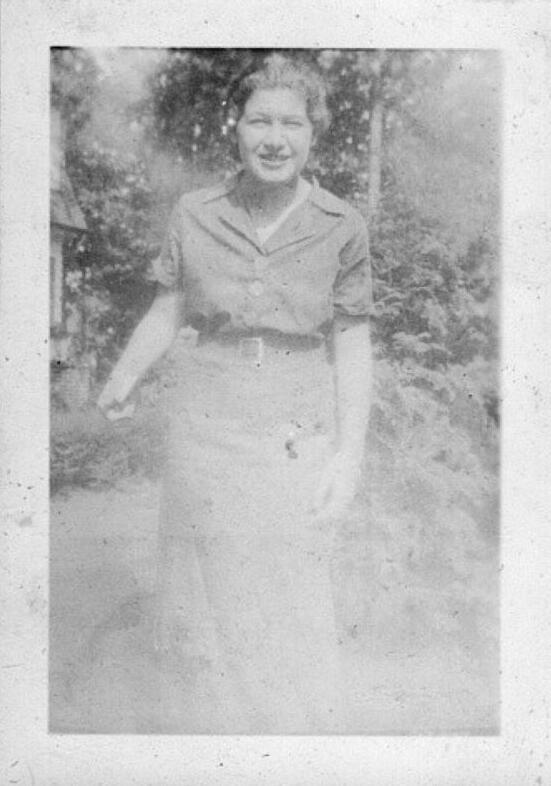 black and white photograph of a woman in a dress in a garden, smiling and squinting slightly