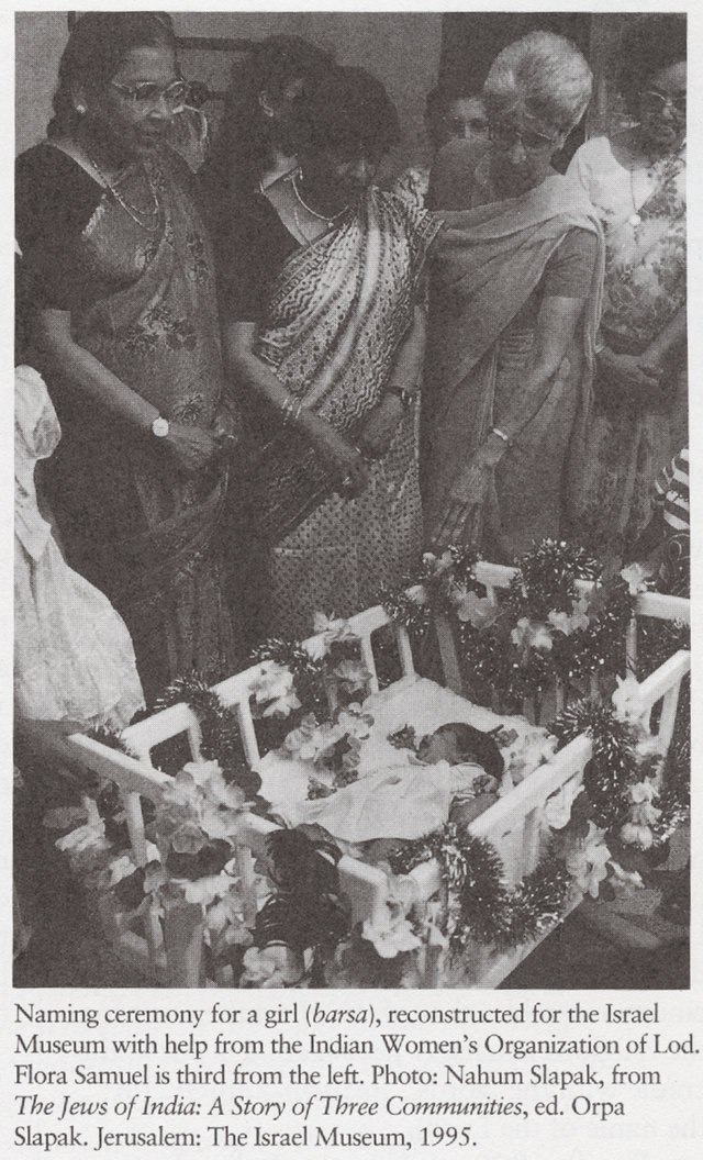 A photograph of a baby in a decorated crib, surrounded by women in saris (including Flora Samuel, third from left), with a caption attributing the photo to the Israel Museum