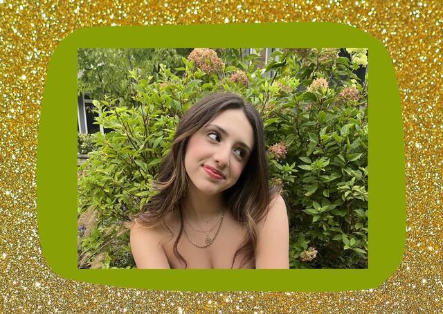 Image of Eva smiling and wearing gold necklaces with flowers in background