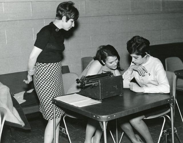 Black and white photo of three women at a table with a typewriter