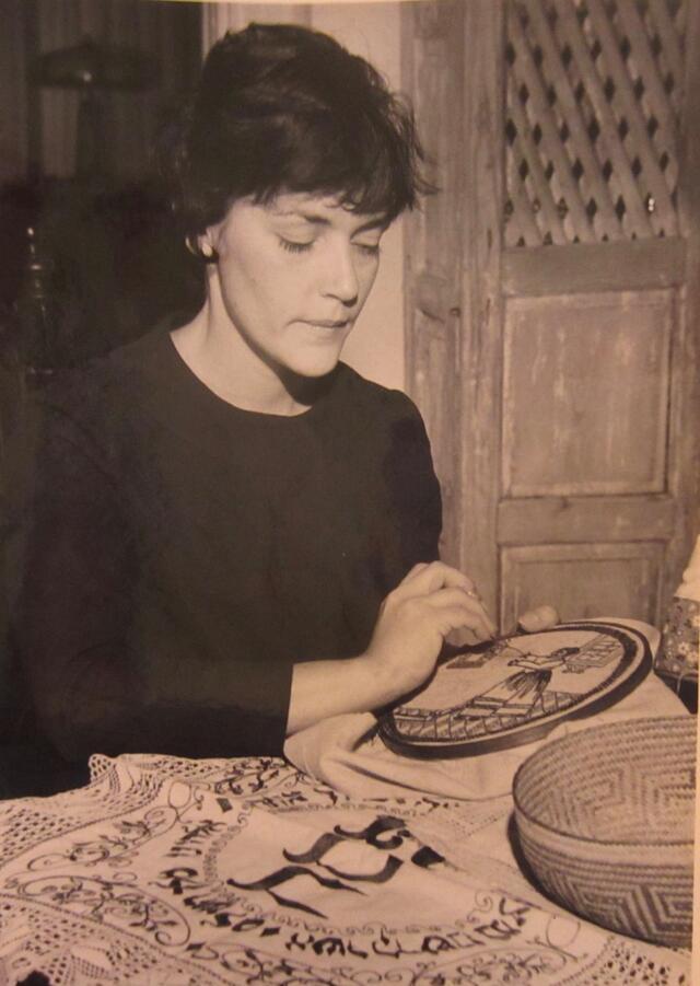 Black and white photograph of a woman embroidering a challah cover