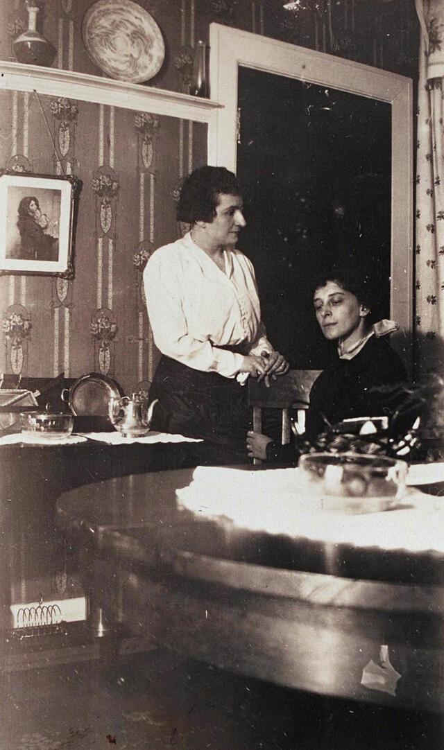 black and white photograph of one woman standing and another sitting at a table