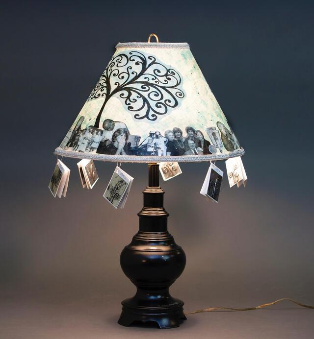 Lampshade adorned with image of a tree, photos of family members, and small dangling books