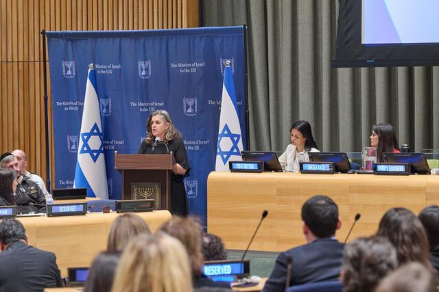 Women speaks at podium with Israeli flags in background