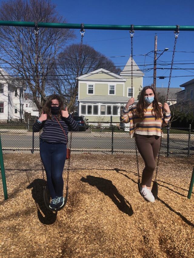 Two teens wearing masks on swings at playground